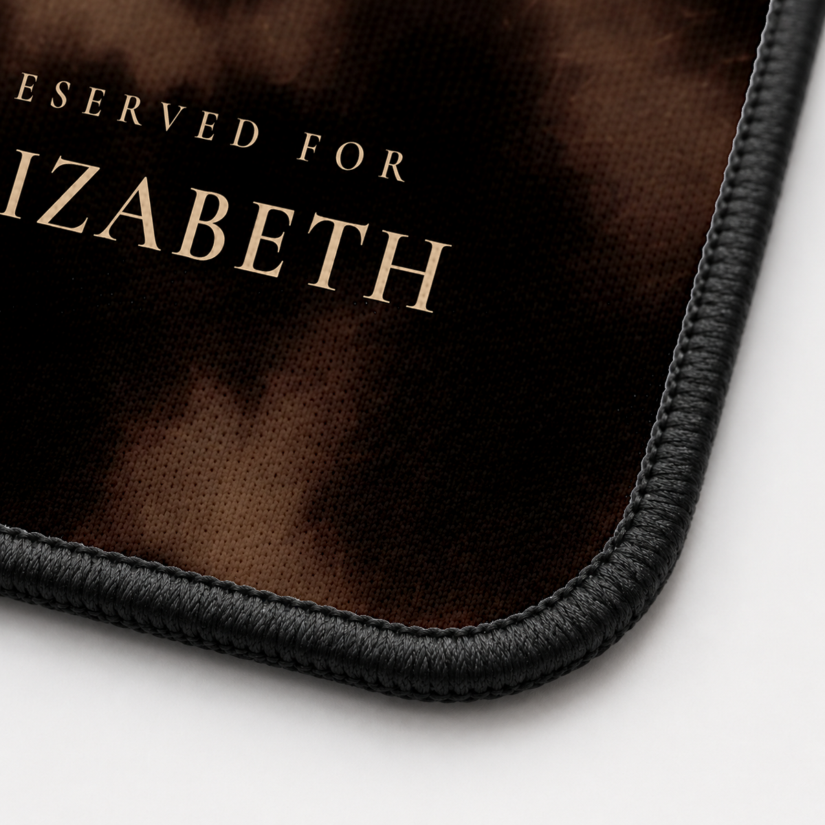 Close-up of the Smoky Tortoise desk mat corner showing the printed surface and the black stitched edge