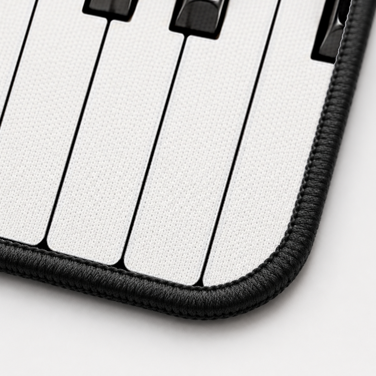 Close-up of the Piano Keys desk mat corner showing the printed surface and the black stitched edge