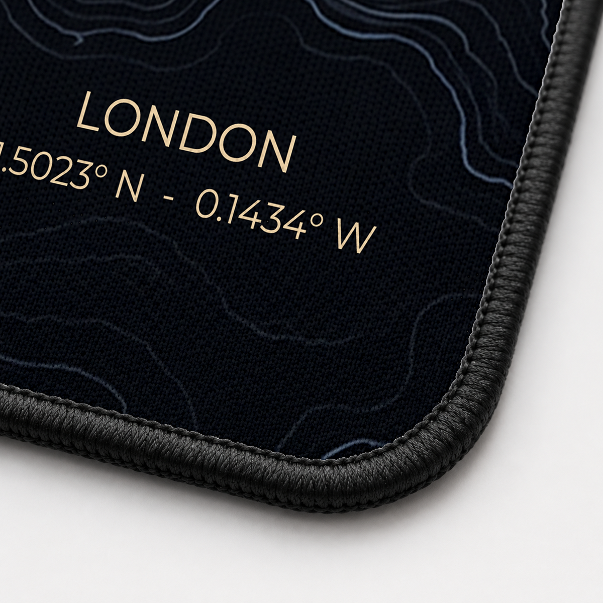 Close-up of the Midnight Topography desk mat corner showing the printed surface and the black stitched edge