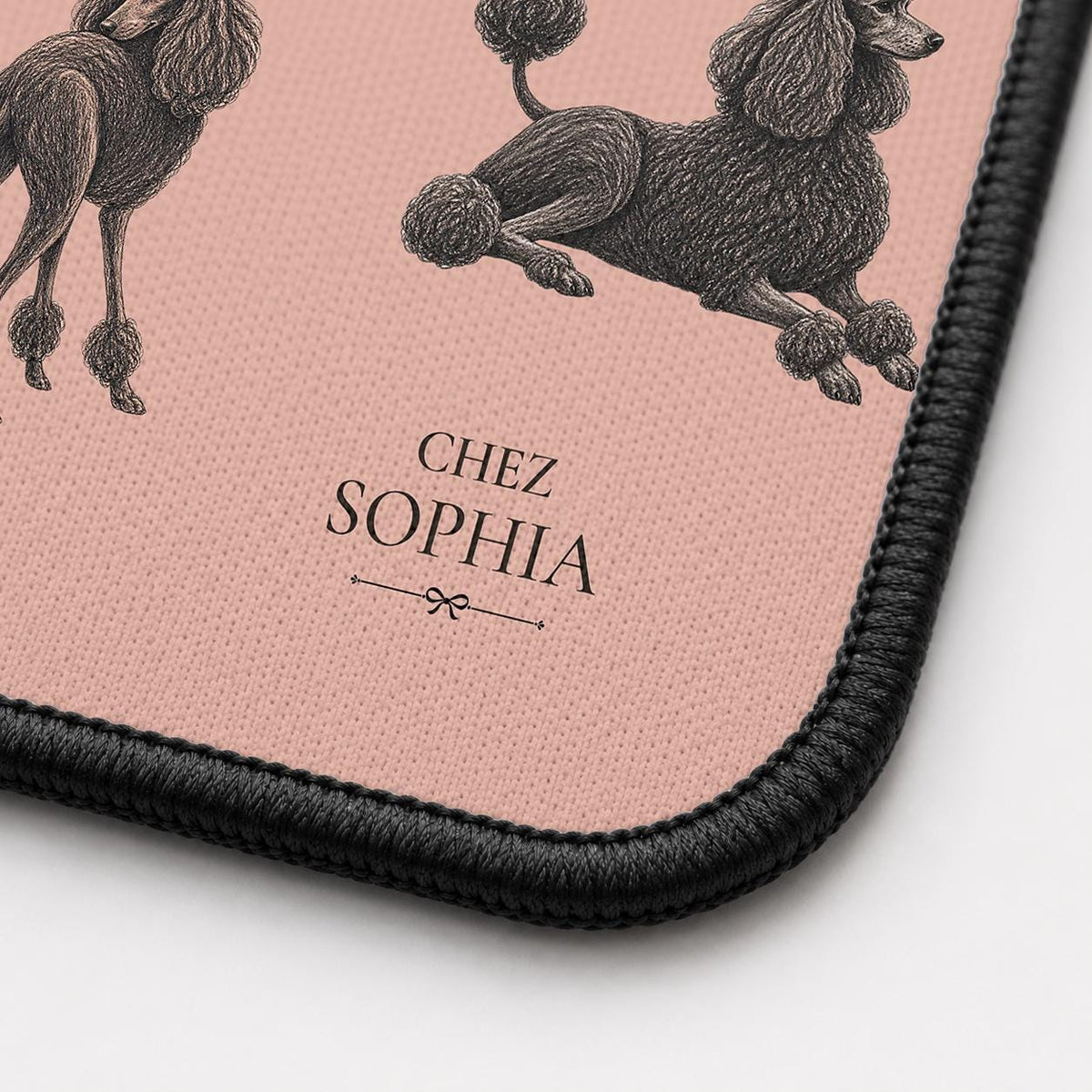 Close-up of the French Poodles desk mat corner showing the printed surface and the black stitched edge